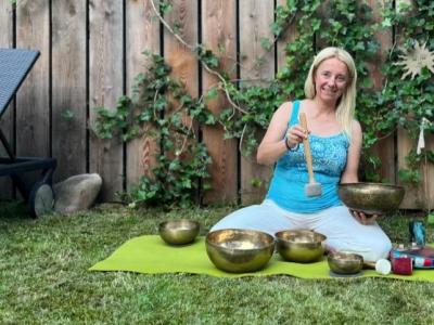 Frau auf grünem Teppich mit tibetischen Schalen im Garten.