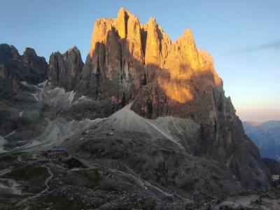 Montagna al tramonto con rifugio, cielo limpido.