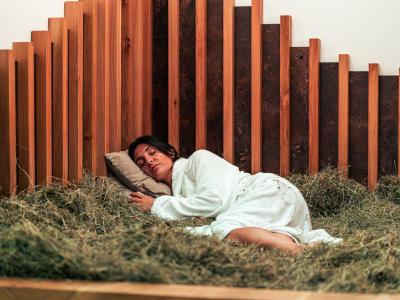 Donna dorme su un letto di fieno in una stanza di legno.