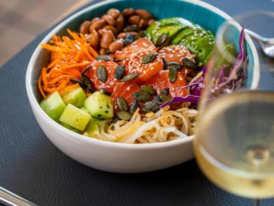 Poke bowl with salmon, avocado, and veggies, served with a glass of wine.