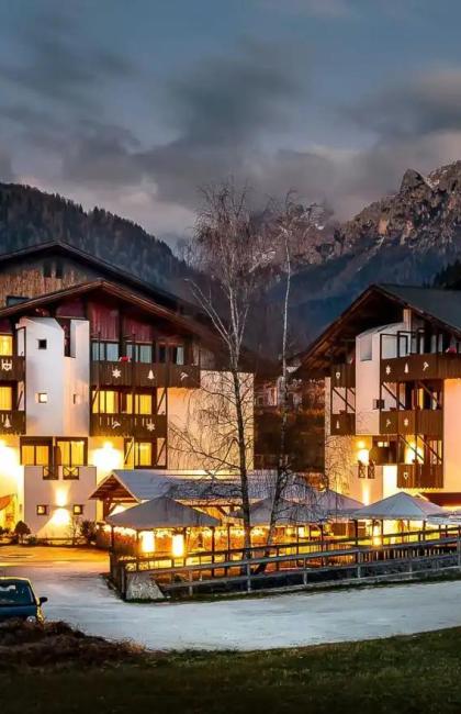 Mountain hotel lit up at night, surrounded by mountains and forests.