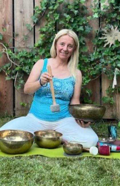 Woman on green mat with Tibetan bowls in garden.