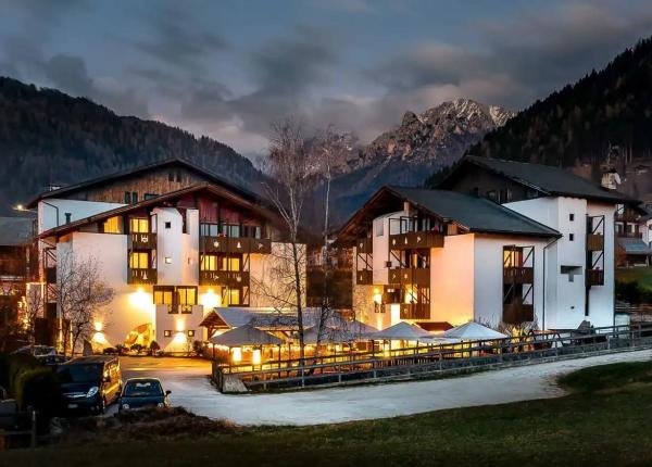 Hotel di montagna illuminato di notte, circondato da montagne e foreste.