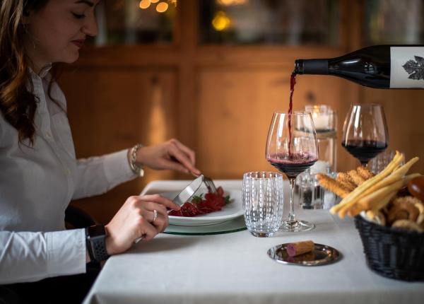 Frau beim Abendessen mit Rotwein und Essen auf einem eleganten Tisch.