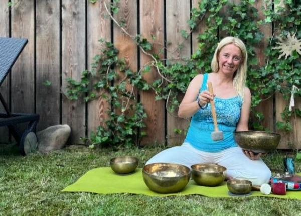 Frau auf grünem Teppich mit tibetischen Schalen im Garten.