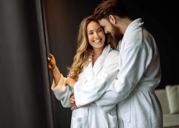 Happy couple in bathrobes embracing near a window.