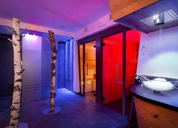 Modern spa with sauna and shower, colorful lighting.