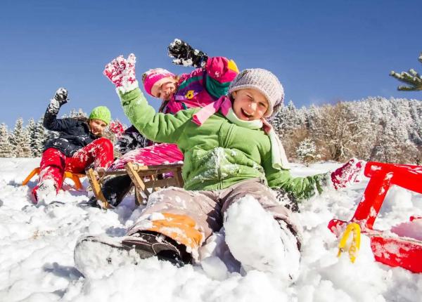 Kinder spielen im Schnee mit Schlitten und haben Spaß an einem Wintertag.