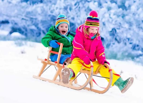 Happy children sledding on the snow in winter.