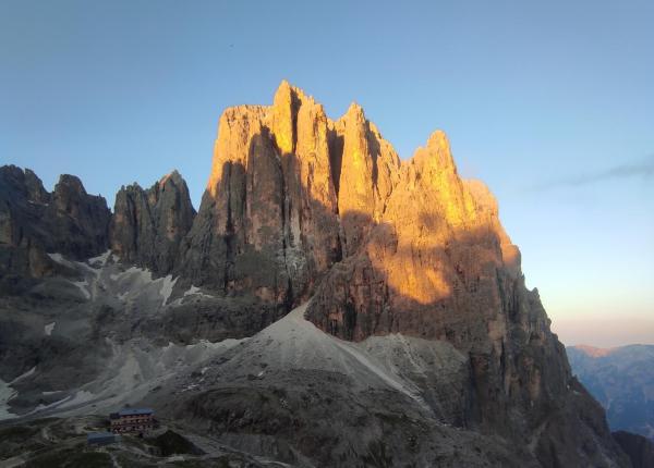 Montagna al tramonto con rifugio, cielo limpido.