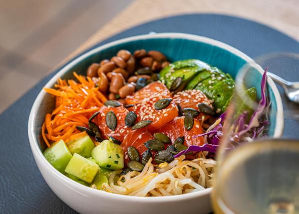 Poke bowl with salmon, avocado, and veggies, served with a glass of wine.