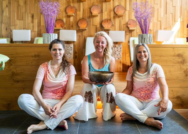 Tre donne sorridenti sedute in un ambiente accogliente con decorazioni in legno.