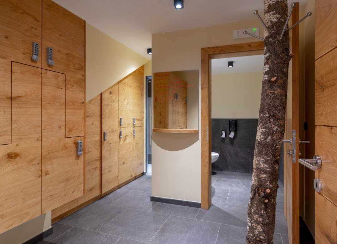 Bagno moderno con pavimento in pietra, armadietti in legno e appendiabiti a forma di tronco.