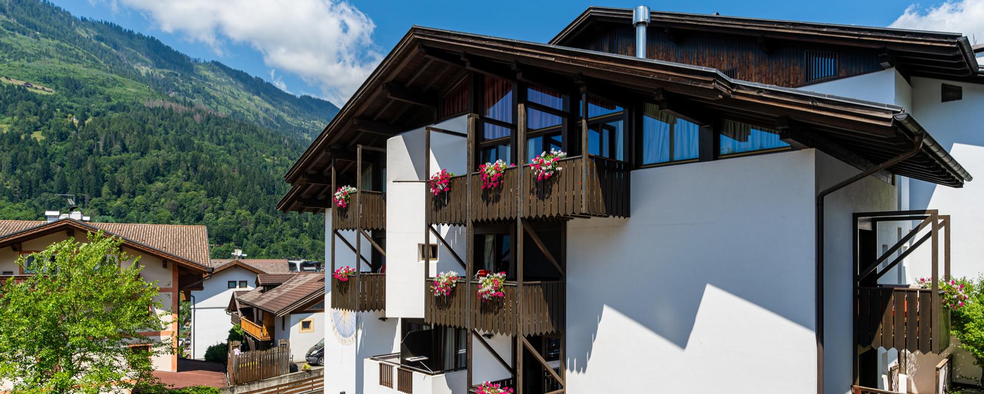 Hotel di montagna con balconi decorati e area relax esterna illuminata di sera.