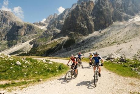 Ciclisti in montagna pedalano su un sentiero ghiaioso circondato da imponenti rocce.