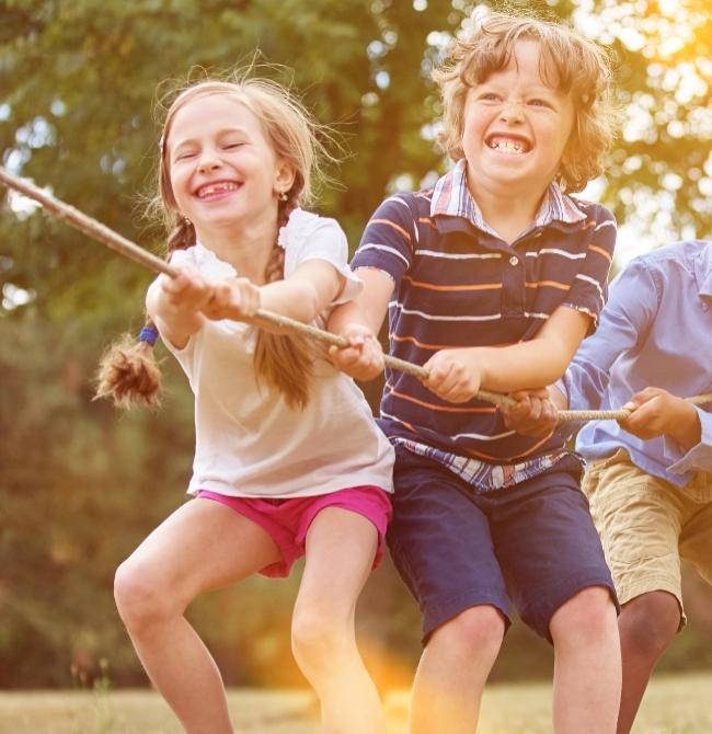 Bambini giocano a tiro alla fune all'aperto, sorridenti e felici.